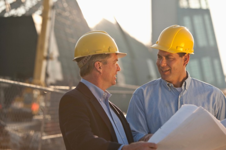 Contractors wearing hard hats and holding construction plans, engaged in conversation at a building site