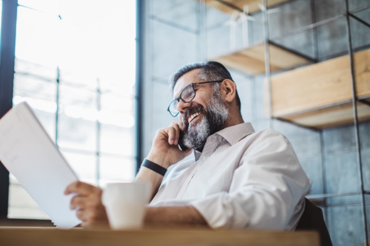 Business professional reviewing paperwork with a cup of coffee in hand, multitasking during a phone call