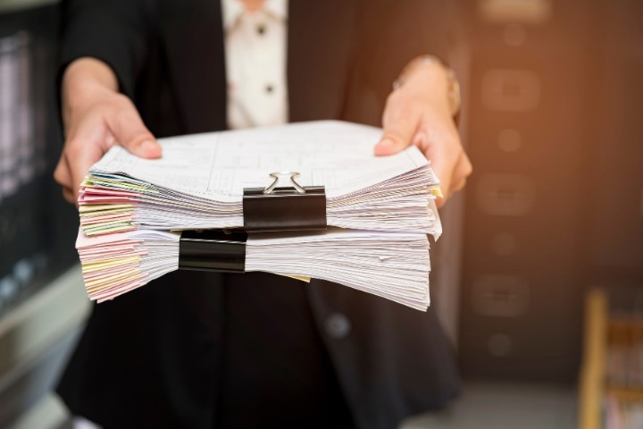 Person holding a large stack of documents, representing the paperwork involved in securing payment and performance bonds for construction