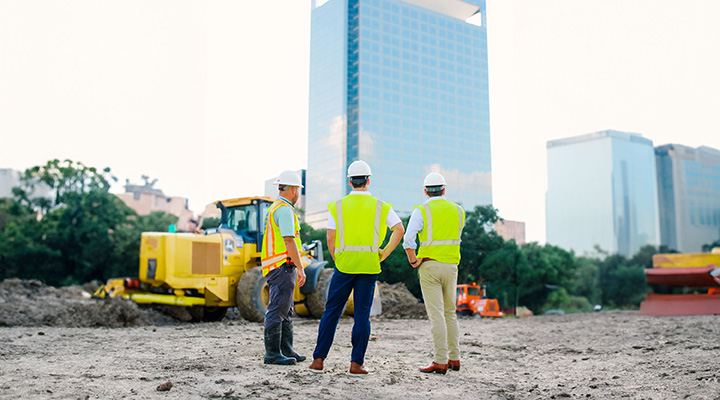 Construction managers in hard hats and safety vests discussing a project site