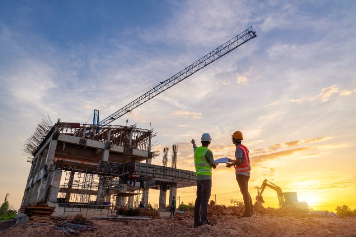 Construction contractors reviewing blueprints near a crane, symbolizing the role of surety bonds in gaining client trust for project opportunities