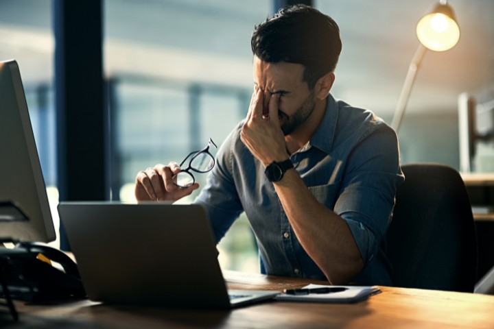 Frustrated contractor at a desk with a laptop, facing project noncompliance issues